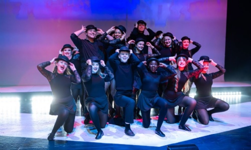 Musical Theatre students doing the same pose holding their hats whilst smiling as part of a performance.
